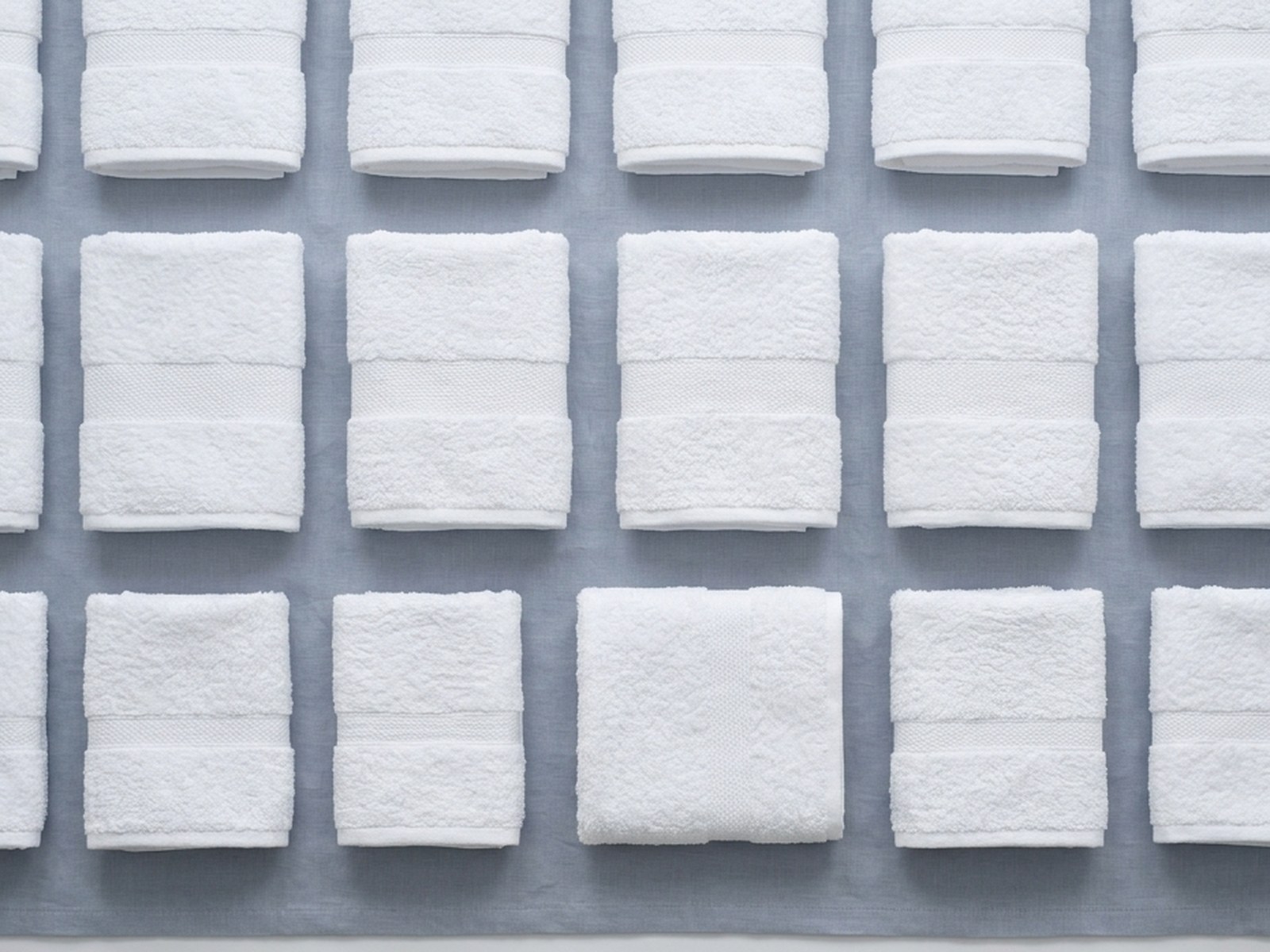 Rows of folded white hotel towels on grey linen
